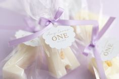 three small white candles wrapped in plastic with purple ribbons and tags that say, one