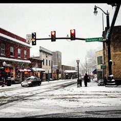 a snowy street with traffic lights and cars on the road in front of buildings that have snow all over them