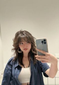 a woman taking a selfie with her cell phone in a bathroom mirror while standing next to a tiled wall