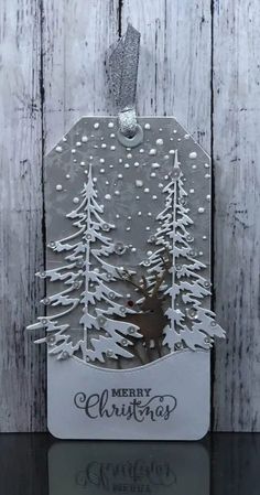 a christmas card with trees and snow on the top, hanging from a wooden background