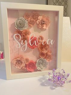 a white frame with pink and grey paper flowers in the shape of sjgoa