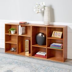 a wooden shelf with books, vase and other items on it next to a rug