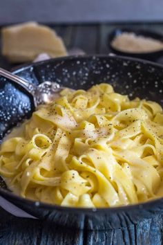 a black bowl filled with pasta on top of a wooden table