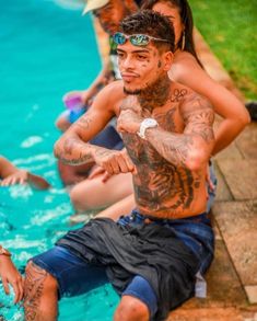 a group of people sitting next to each other near a swimming pool with tattoos on their arms