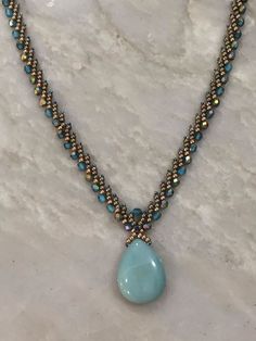 a necklace with blue beads and a tear shaped stone hangs from a marble counter top