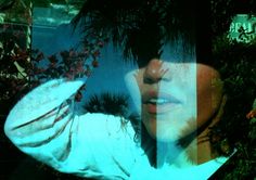 a woman with her hand on her head and trees in the background, through which she is wearing a white shirt