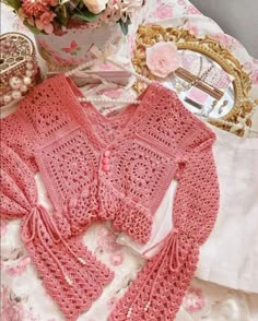 a crocheted pink sweater sitting on top of a bed next to a potted plant