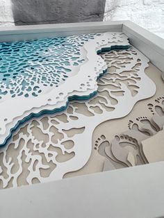 an intricate paper cut artwork with footprints on the beach