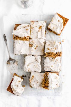 carrot cake with cream cheese frosting on a white surface next to a glass of water