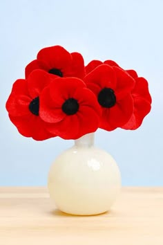 three red flowers in a white vase on a table