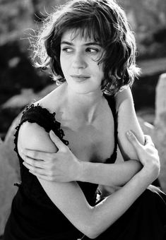 black and white photograph of a woman with her arms around her chest, sitting on a rock