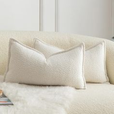 two white pillows sitting on top of a couch next to a book and remote control