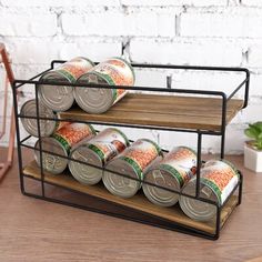 two tiered spice rack holds cans of canned food and sits on a wooden table next to a potted plant