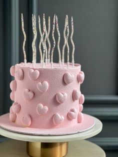 a pink cake with lots of hearts on it and candles sticking out of the top