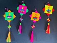 four colorful kites hanging from strings on a black background with the words happy diwali written below them