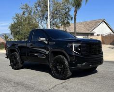 the black truck is parked on the street in front of some palm trees and houses