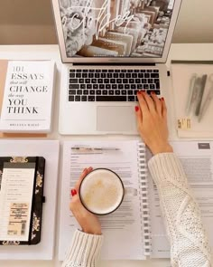 a woman is working on her laptop while holding a cup of coffee and reading the book