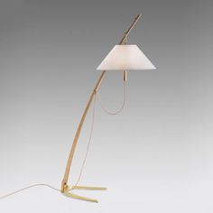 a floor lamp with a white shade on the top and a gold metal base, in front of a gray background