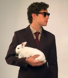 a man in a suit and sunglasses holding a white rabbit inside his lapel pocket