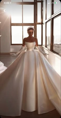 a woman in a white wedding dress standing by a window with her hands on her hips