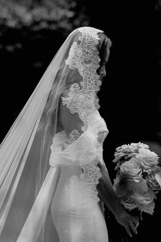 a woman in a wedding dress and veil walking with her bouquet on the other side