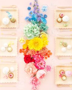 an arrangement of colorful flowers and jewelry laid out on a pink surface with white trays