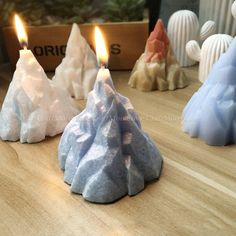 three candles sitting on top of a wooden table next to small rocks and snow covered trees