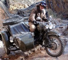 a man riding on the back of a motorcycle down a dirt road next to rocks