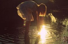 a woman is standing in the water with her hands on her knees as the sun goes down