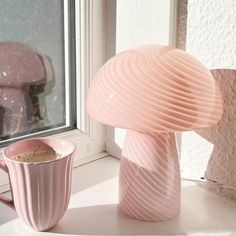 a pink vase sitting next to a cup on a window sill