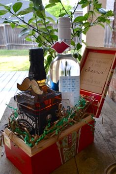 a wooden table topped with an open box filled with liquor and other items next to a potted plant