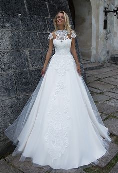 a woman in a white wedding dress standing next to a stone wall with her hands on her hips