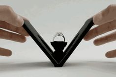 two hands holding an object in the shape of a triangle with a ring on it