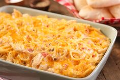 a casserole dish with chicken and cheese in it on a table next to bread