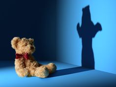 a teddy bear with a red bow sits in front of a shadow of a man