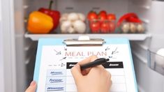 a person is writing on a clipboard in front of an open refrigerator with vegetables