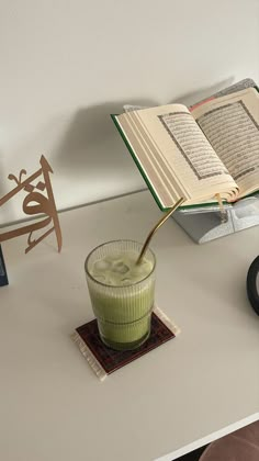 an open book sitting on top of a desk next to a glass filled with liquid