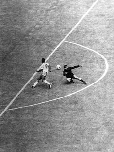 two men playing soccer on a field with one kicking the ball and another running after it