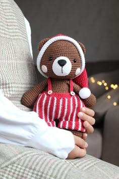 a person holding a stuffed teddy bear in their hand on a couch with christmas lights behind them