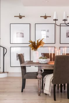 a dining room table with chairs and pictures on the wall in front of it,