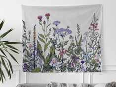 a tapestry hanging on the wall above a couch in a living room with flowers and plants