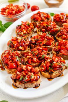 several pieces of bread with tomatoes on them sitting on a white plate next to some green leaves