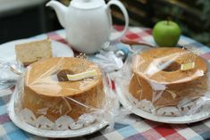 two cakes sitting on top of plates covered in plastic wrapper next to an apple