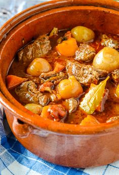 beef stew with potatoes and carrots in a clay pot on a blue checkered table cloth