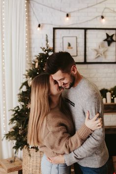 a man and woman hugging in front of a christmas tree with lights on the wall