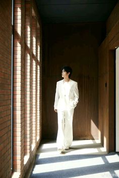 a man in a white suit and sunglasses walking down a hallway with sun shining through the windows