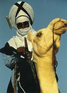 a man riding on the back of a camel wearing a white turban and sunglasses