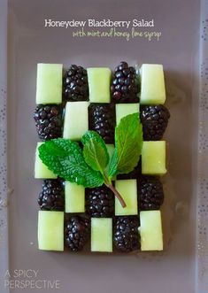 a plate with blackberries, kiwis and mint leaves on it that is cut into squares