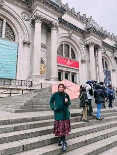 a woman holding an umbrella standing on steps in front of a large building with columns