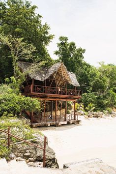 a house on the beach with trees in the back ground and water behind it, surrounded by vegetation